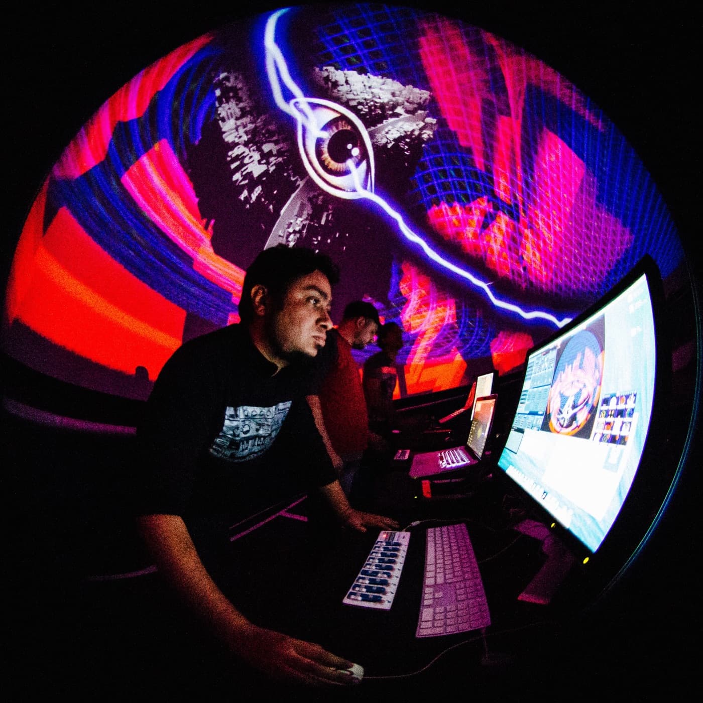 A VJ at the controls, lit by a red and blue dome projection, shot through a fisheye lens