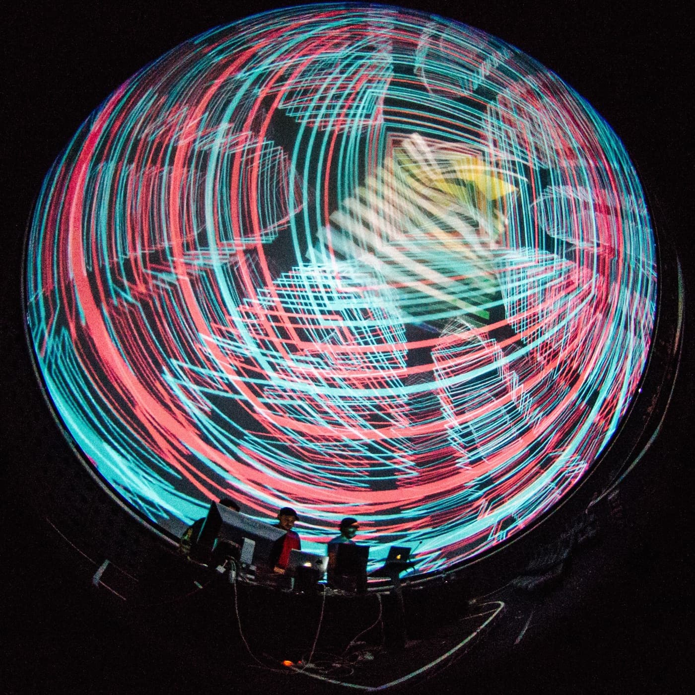 Red and cyan light trails across a full dome, three VJs at the desk beneath